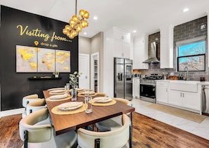 A modern kitchen with white cabinets, stainless steel appliances, and a dining area with a wooden table and chairs. - Dallas escape - Rooftop + Hot tub - Vintage Arcade (Dallas)