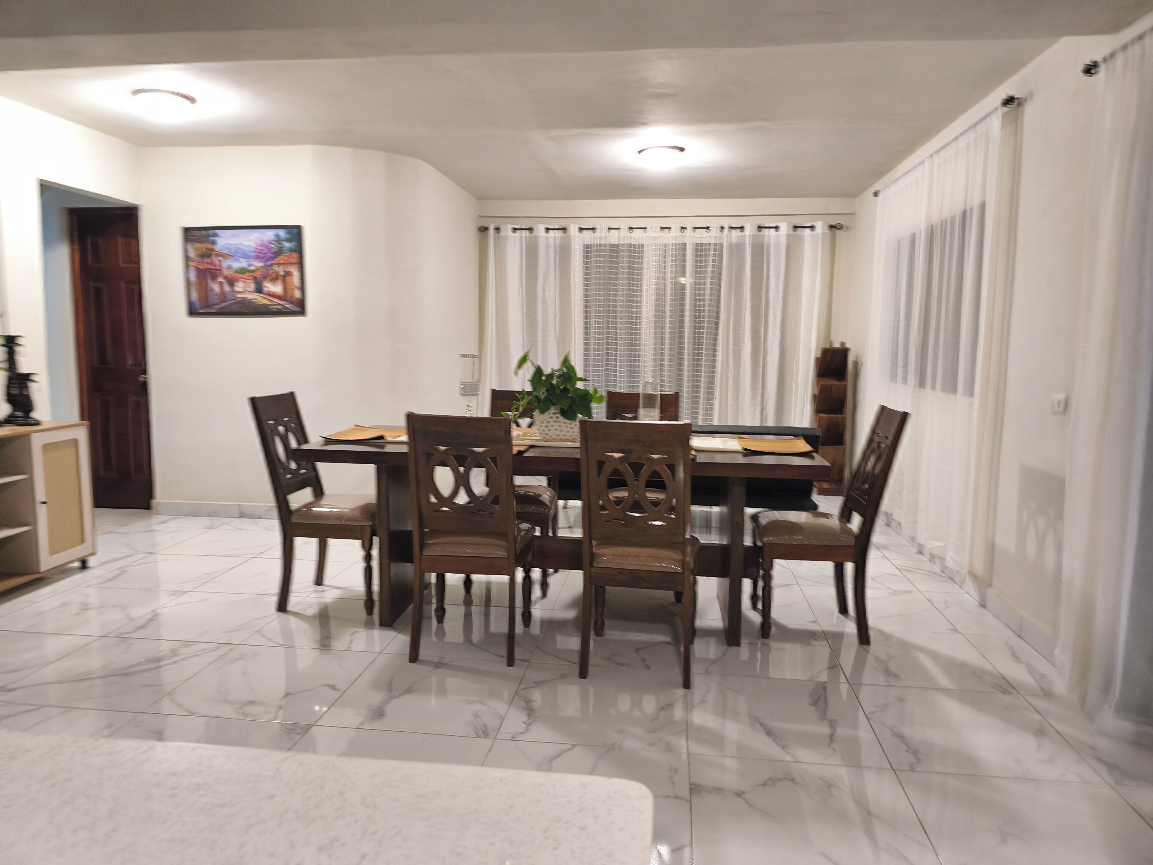 A dining area with a round table, six chairs, and a potted plant.