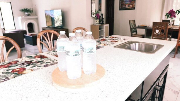 A kitchen with a white countertop, a wooden cutting board, and bottles of Great Value drinking water. - Mansion bosque sereno luxury (juayua)