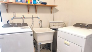 A laundry room with two washing machines, a sink, and a shelf with cleaning supplies. - Mansion bosque sereno luxury (juayua)