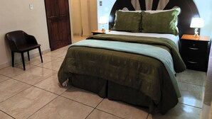 A bedroom with a bed, two bedside tables with lamps, a chair, and a door. - Mansion bosque sereno luxury (juayua)
