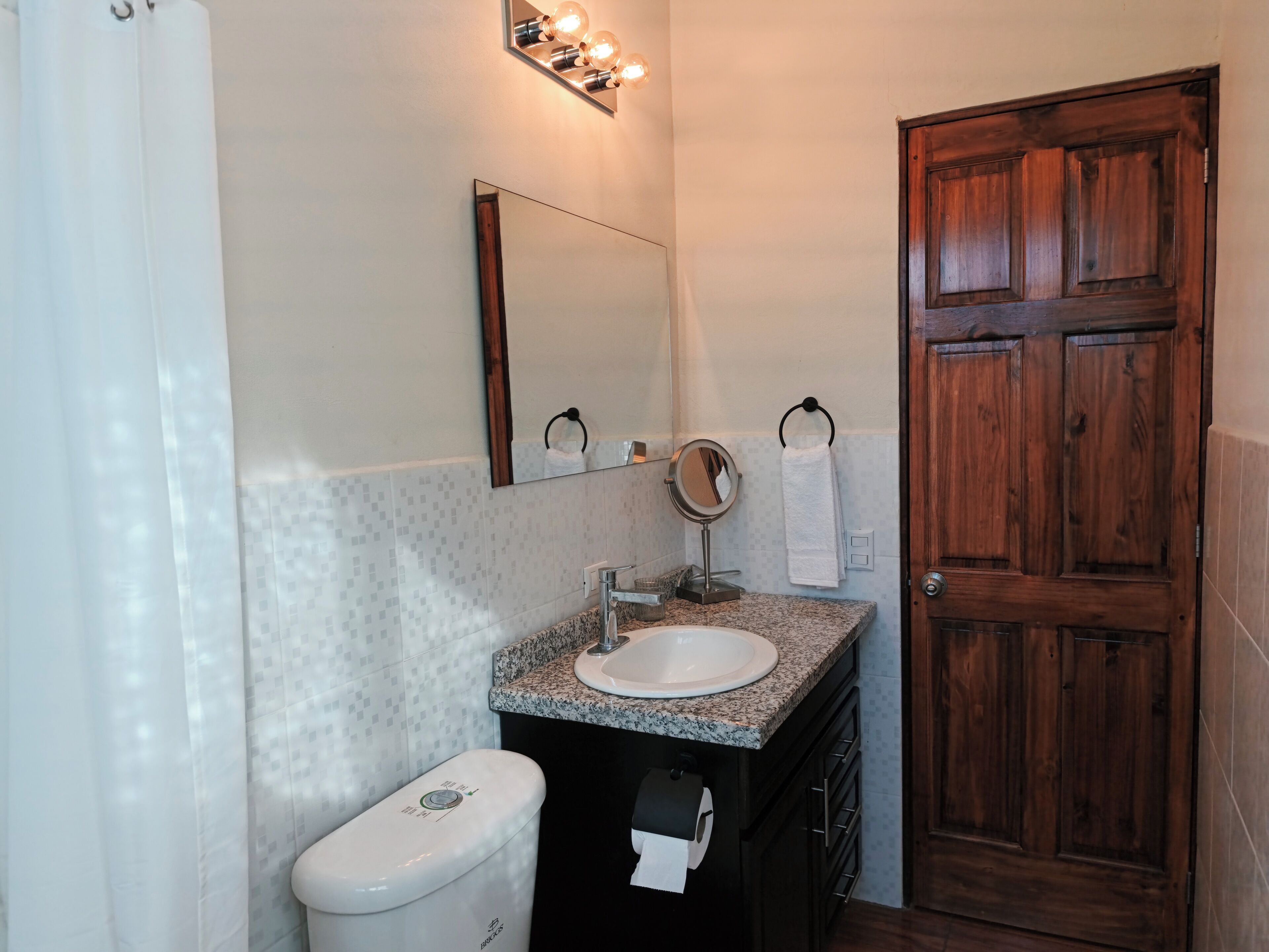 A bathroom with a white toilet, a sink with a mirror above it, and a wooden door.