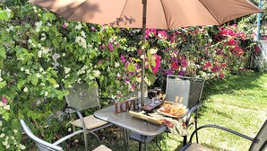 An outdoor patio with a table and chairs under a large umbrella, surrounded by lush greenery and vibrant flowers. - Mansion bosque sereno luxury (juayua)