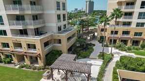 A multi-story residential building with balconies, a central courtyard with outdoor seating, and a view of a body of water and surrounding buildings. - Luau 6312 Cozy Studio Retreat | Pool, Tram, Beach | Skis & Seas (Miramar Beach)