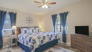 Ein Schlafzimmer mit Bett, Deckenventilator, Fernseher und Kommode.