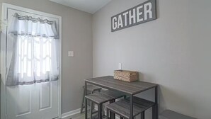 Ein kleiner Raum mit einer Tür, einem Tisch mit zwei Stühlen und einem Schild mit der Aufschrift 'GATHER'.