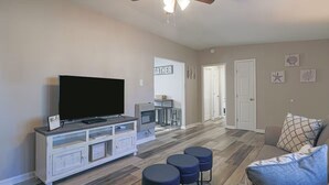 Ein Wohnzimmer mit Fernseher auf einem weißen Schrank, Deckenventilator und einem 'GATHER'-Schild an der Wand.