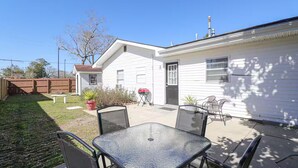 Ein Wohnhaus mit einer Terrassenfläche, die einen Glastisch, Stühle, einen Grill und einen kleinen Garten mit Blumentöpfen zeigt.