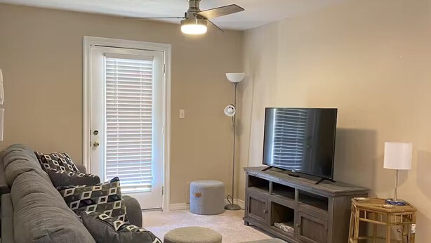 A living room with a gray sectional sofa, a television on a wooden stand, a ceiling fan, and a door with blinds. - Waterfront Escape in Bay St. Louis (Bay St. Louis)