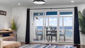 A living room with a sofa, a coffee table, and a view of the ocean through large sliding glass doors. - 🌅 Sunset+Kayak | Private Beach House | M22 ➠ 7633 (Traverse City)