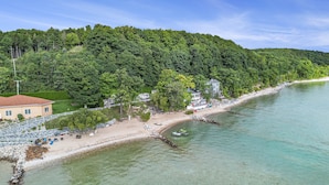 A coastal property with a beach, a house, and a forested hill. - 🌅 Sunset+Kayak | Private Beach House | M22 ➠ 7633 (Traverse City)