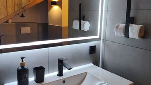 A modern bathroom with a white sink, black faucet, and soap dispenser. There is a towel rack with a towel hanging on it, and a mirror with integrated lighting. - Vacation apartment in Burghausen - castle magic near the world's longest castle (Burghausen)