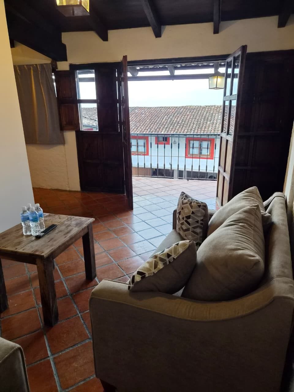 Una stanza con un divano, un tavolino con bottiglie d'acqua e vista su un edificio con finestre rosse attraverso porte aperte.