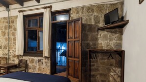Ein rustikales Zimmer mit Bett, Holzmöbeln, einem an einer Ablage montierten Fernseher und einer Steinwand.