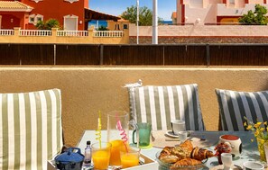 A balcony with striped cushions, a table with breakfast items, and a view of colorful buildings. - Nice home in La Manga (San Javier)