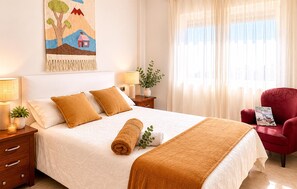 A neatly made bed with a white and brown blanket, two pillows, a rolled towel, a small plant, and a red armchair. - Nice home in La Manga (San Javier)