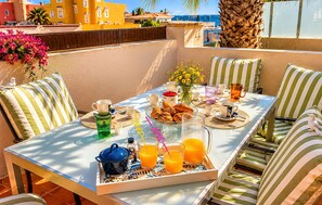 A sunlit terrace with a table set for breakfast, striped cushions, and a view of the sea. - Nice home in La Manga (San Javier)