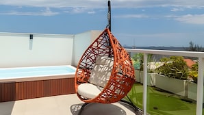 Ein Hängestuhl mit weißem Kissen auf einem Balkon mit Pool und Meerblick.