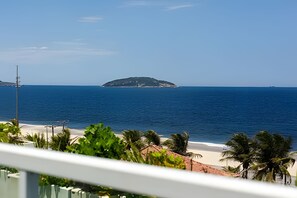 Blick auf einen Strand mit einer kleinen Insel im Hintergrund, einem klaren Himmel und etwas Grün im Vordergrund.