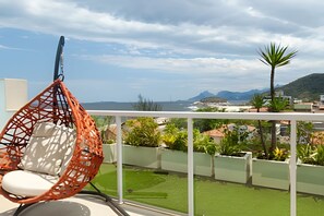 Ein Balkon mit einer Hängematte, Blick auf das Meer und einer grünen Rasenfläche.