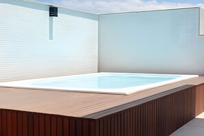 Ein moderner Außenbereich mit Whirlpool, einer Holzterrasse und einer hellen Wand im Hintergrund.