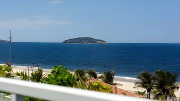 A beach view with a small island in the distance, a clear sky, and some greenery in the foreground.