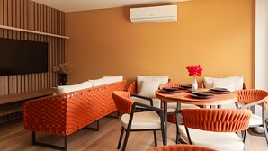 Un salon moderne comprenant un canapé, des fauteuils, un téléviseur et un appareil de climatisation.