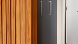 Ein Zimmer mit einer Wand aus Holzpaneelen, einem dunkelgrauen Schrank mit zwei Griffen und einer weißen Tür zu einem anderen Raum.