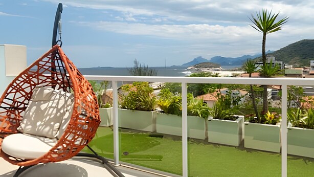 Un balcon avec un fauteuil suspendu, une vue sur la mer et une pelouse verdoyante.