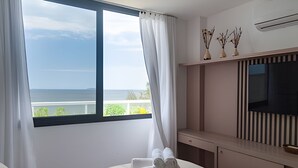 Ein Hotelzimmer mit großem Fenster, einem Bett, einem Fernseher und einer kleinen Ablage mit Dekoration.