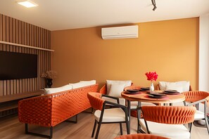 Ein modernes Wohnzimmer mit einer Couch, Sesseln, einem Fernseher und einer Klimaanlage.