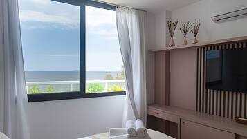 A hotel room with a large window, a bed, a TV, and a small shelf with decorative items.