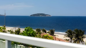 Une vue sur la plage avec une petite île au loin, un ciel dégagé et quelques éléments de végétation au premier plan.