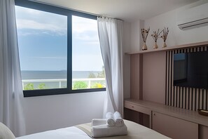 Ein Hotelzimmer mit großem Fenster, einem Bett, einem Fernseher und einer kleinen Ablage mit Dekoration.