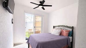 Ein Schlafzimmer mit Bett, Deckenventilator, Fenster und einer Tür, die auf einen Balkon führt.