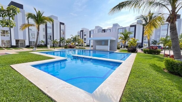 Ein modernes Hotel mit rechteckigem Pool, umgeben von gepflegtem Rasen und Palmen.