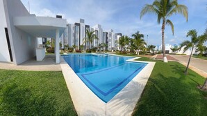 Ein modernes Hotel mit Swimmingpool, Palmen und einem gepflegten Rasen.