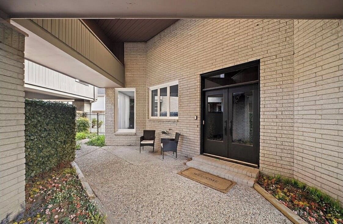 A covered outdoor area with a brick wall, a door, and a small seating area with two chairs and a table.