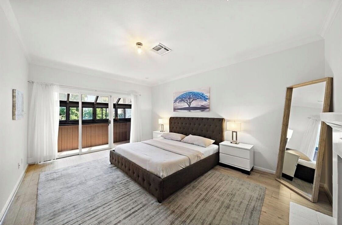 A modern bedroom with a large bed, a nightstand, a mirror, and a painting on the wall.