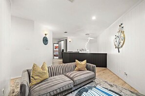 A modern living room with a grey sofa, a patterned rug, and a kitchen area in the background. - Luxe-Galleria. Terrific 3-bedroom house with AC in vibrant Houston (Houston)