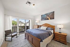 A bedroom with a bed, two bedside tables, a chair, a large window, and a ceiling vent. - Luxe-Galleria. Terrific 3-bedroom house with AC in vibrant Houston (Houston)