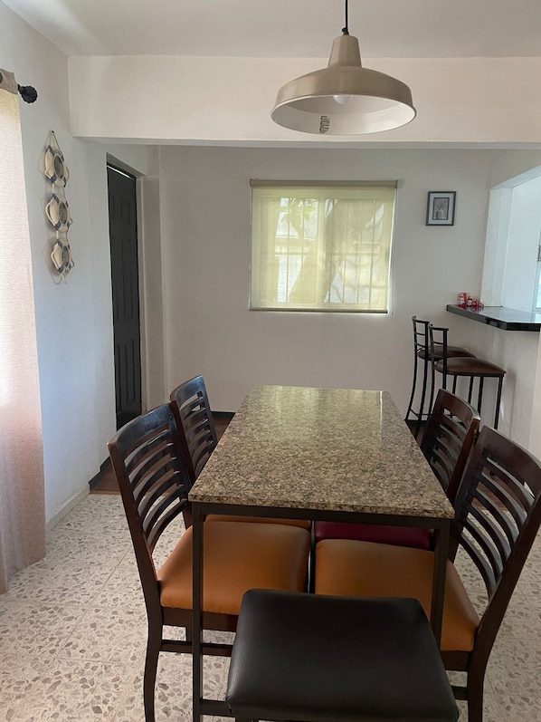 A dining area with a granite table, six wooden chairs, and a pendant light.