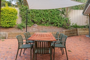 Eine Terrasse mit Holztisch und -stühlen, umgeben von einem Backsteinboden und einer Hecke.