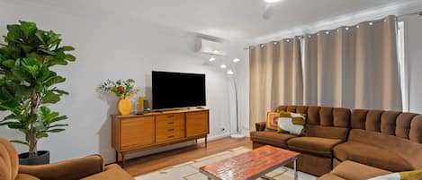 A modern living room with a sofa set, a television on a wooden cabinet, a potted plant, and a ceiling fan.