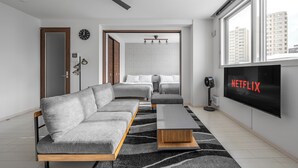 A modern living room with a grey sofa, a wooden coffee table, and a flat-screen TV displaying 'NETFLIX'. - GRANDIA 202 (Sapporo)