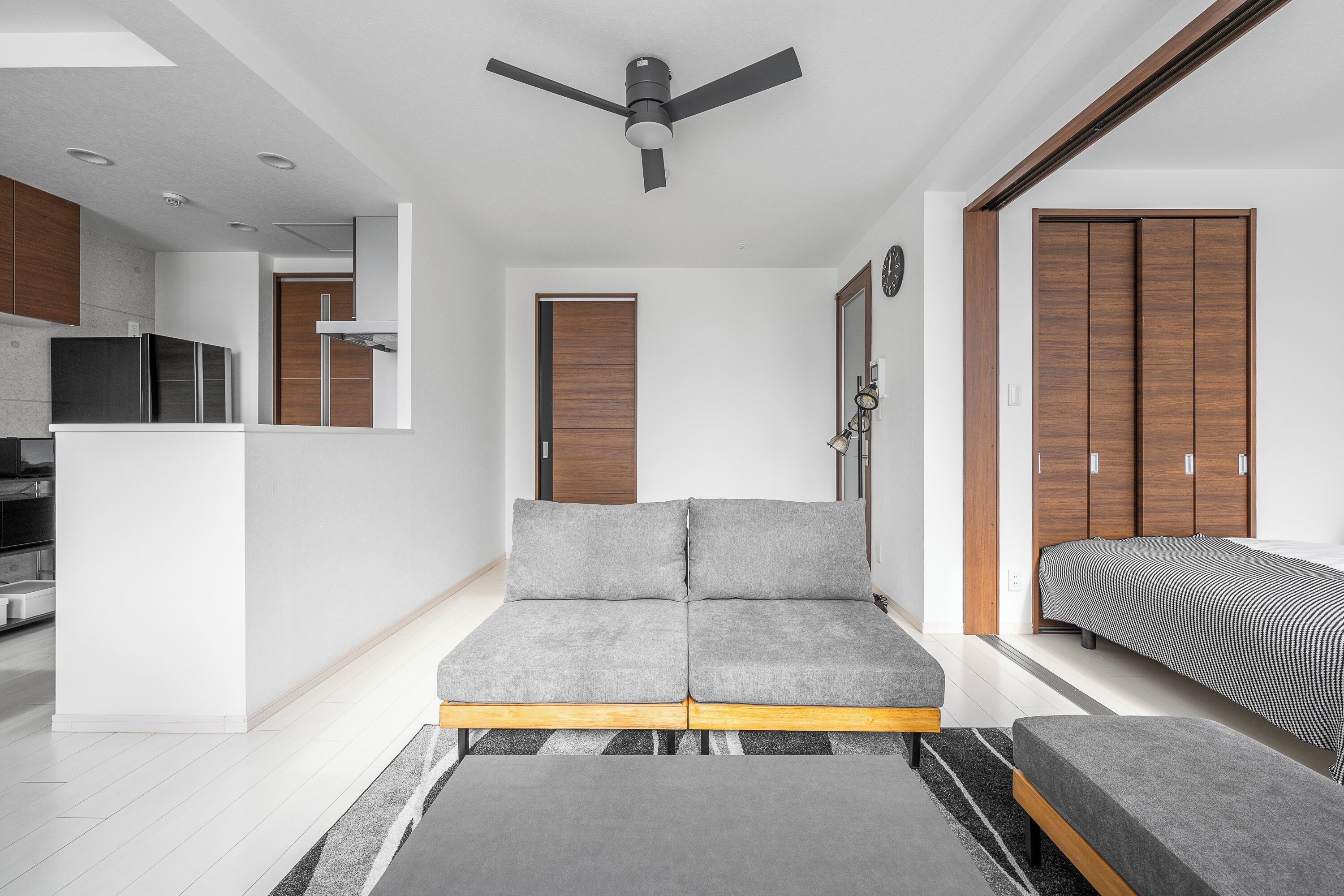 A modern living room with a sofa, a bench, a ceiling fan, and a kitchen area visible in the background.