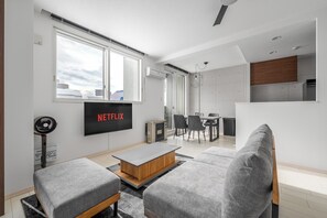 A modern living room with a flat-screen TV, grey sofas, a wooden coffee table, and a dining area with chairs. - GRANDIA 202 (Sapporo)