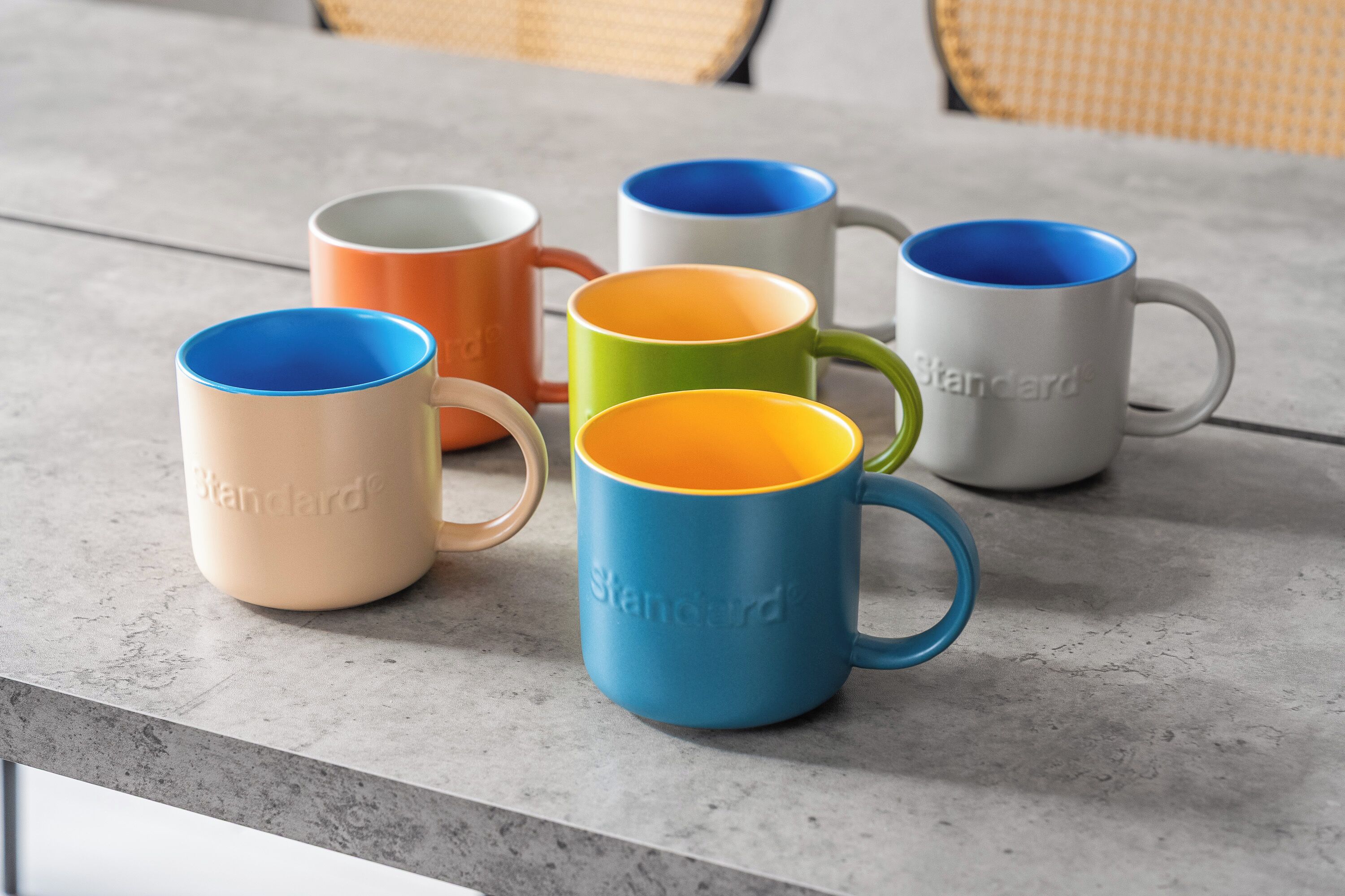 Six Standard branded mugs in various colors arranged on a grey countertop.