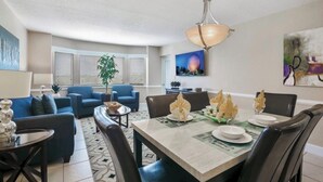 A modern living room with a dining area, featuring a chandelier, sofas, a coffee table, and a dining table set for four. - Summer Disney Getaway, 2BR/2BA, sleeps 6, June 18-21, Resort Pool (Kissimmee)
