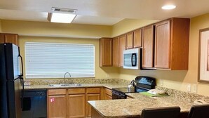 A kitchen with wooden cabinets, a granite countertop, a built-in microwave, and a black dishwasher. - Summer Disney Getaway, 2BR/2BA, sleeps 6, June 18-21, Resort Pool (Kissimmee)